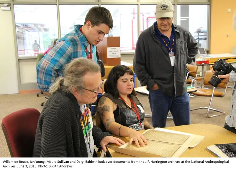 Two people sitting, looking at archival documents while two other people stand behind them looking over.