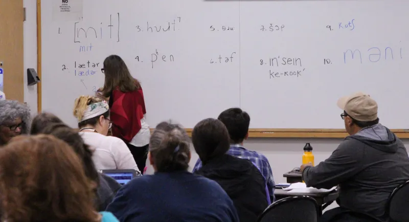 Group of people looking at a white board with a woman writing.