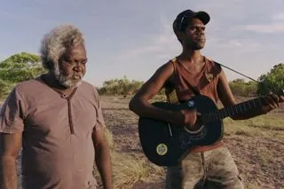 Two men standing, one playing a guitar.
