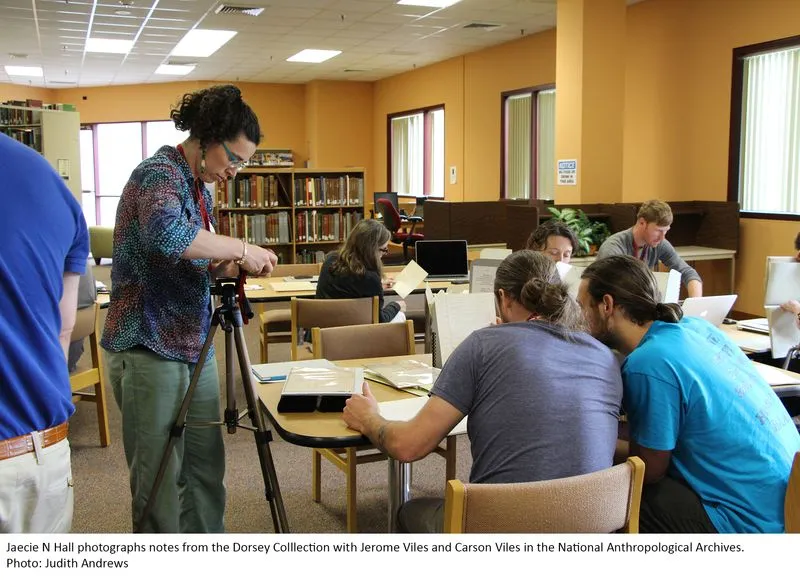 Groups of people sitting at desks looking over archival materials.