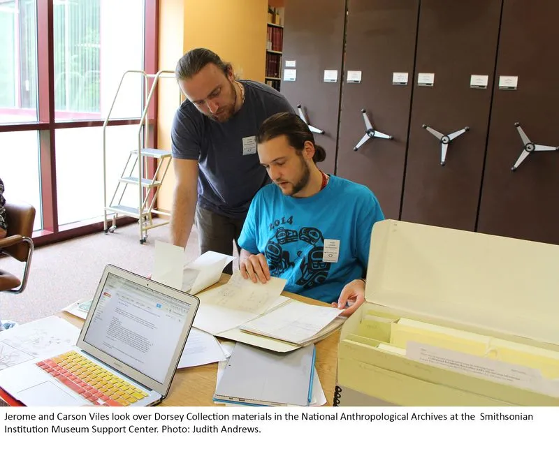 Two people looking at archival materials; one is sitting, one is standing.
