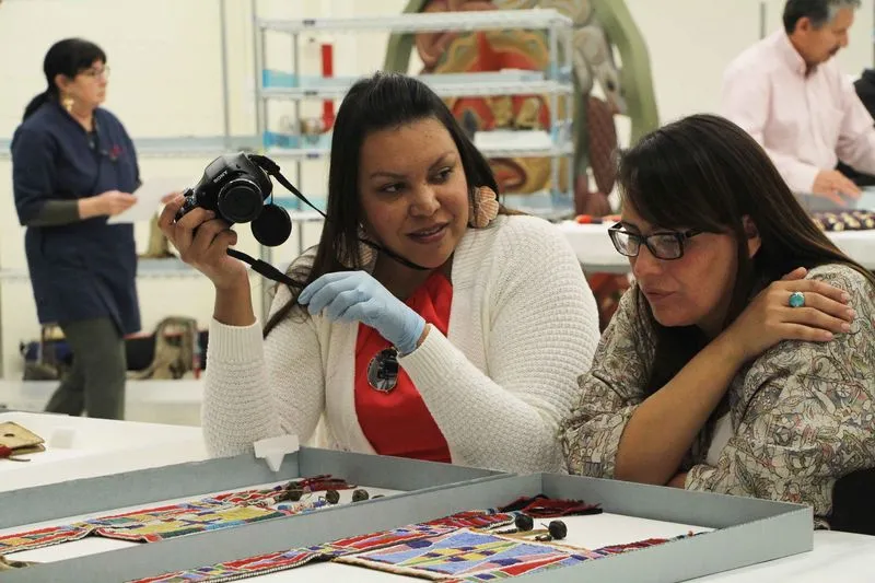 Two women looking at Crow beadwork; one is holding a camera.