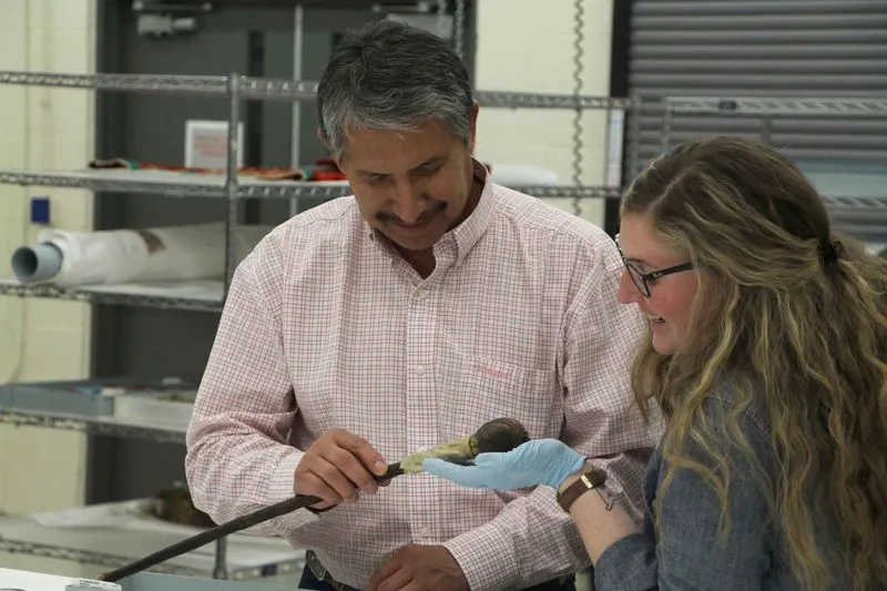 Two people holding and discussing a war club in a collections space.