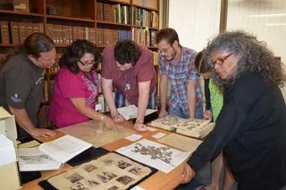 Group of people crowded around various archival materials on a table.