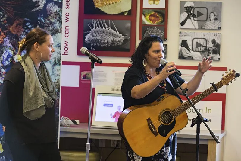 Woman with a guitar speaking into a microphone.