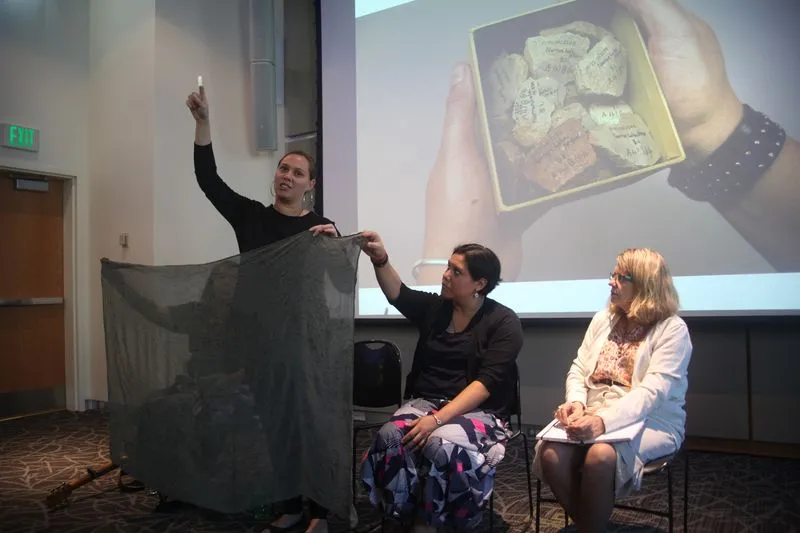 Woman holding up a scarf, spread out; image of fragmented ceramics on a screen in the background.