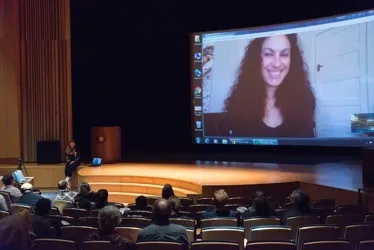Audience looking at a woman on a projector screen.