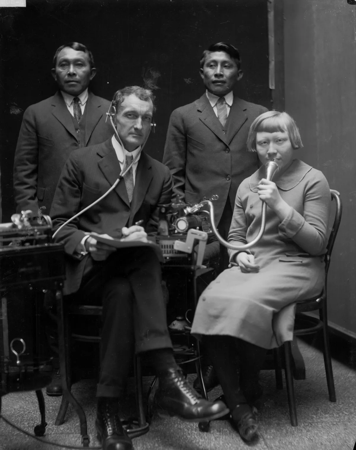 1924 photo of John Peabody Harrington posing with three Tule, or Kuna, people while making dictaphone recordings of Kuna language and songs.