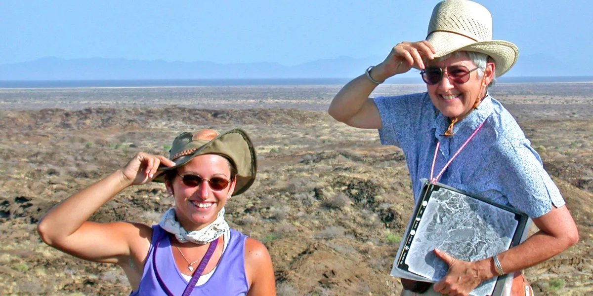Photo of two women looking at the camera holding their hats doing fieldwork