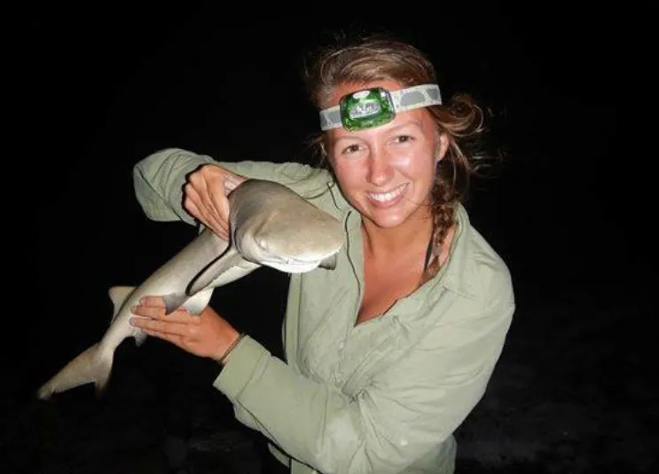 A woman wearing a headlamp and holding a small shark.