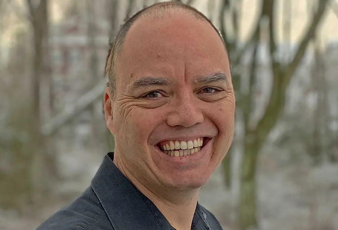 John Cook, smiling, standing in front of some woods.