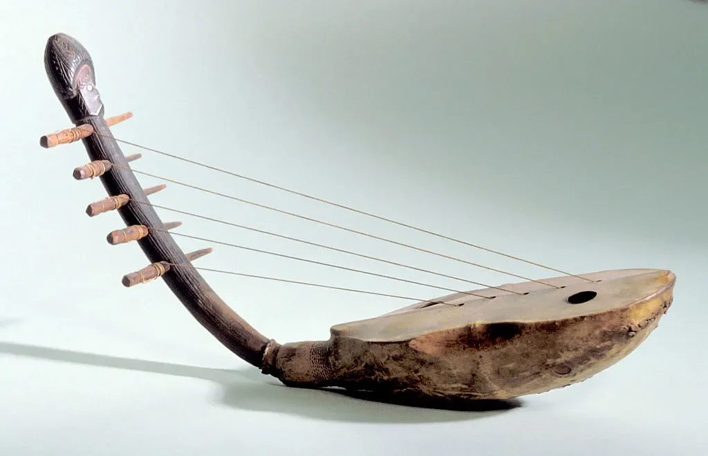 A harp that consists of a wooden sound box with an animal skin stretched across it, a curved wooden neck attached to the sound box to which the strings are fixed with five tuning pegs. An anthropomorphic head crowns the top of the neck.