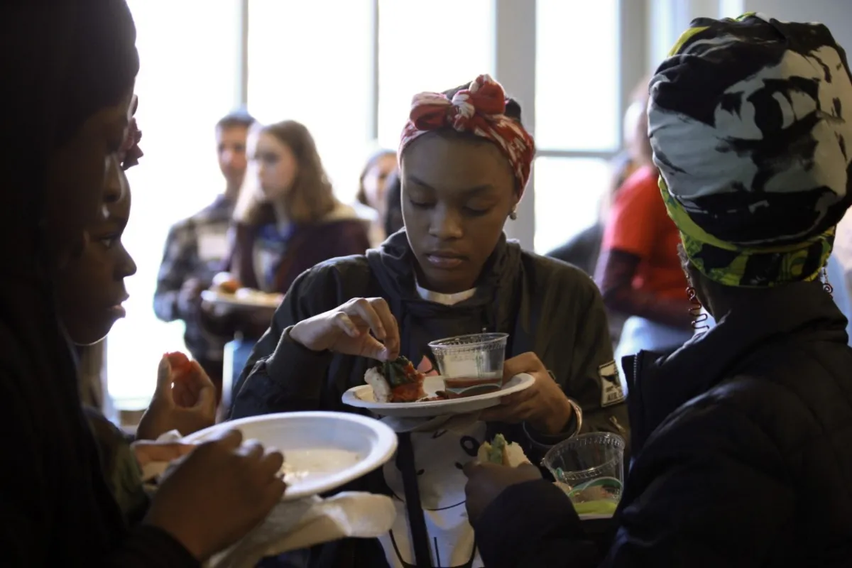 A teenage girl holding a paper plate and picking up a piece of food from it.