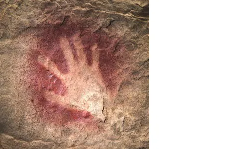 A white handprint on a stone wall. The handprint has red pigment or paint around it.