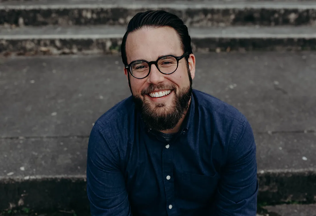 A man in a navy blue shirt, sitting on some steps, smiling.