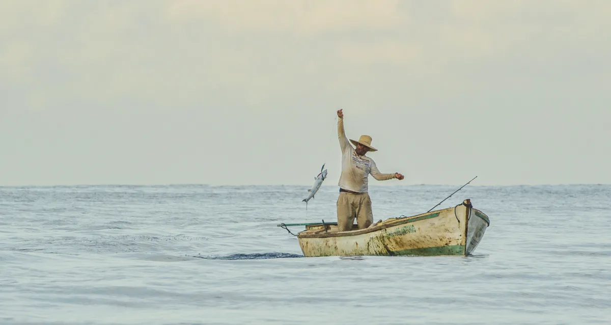 A fisherman casting a net from a small boat on the ocean. 