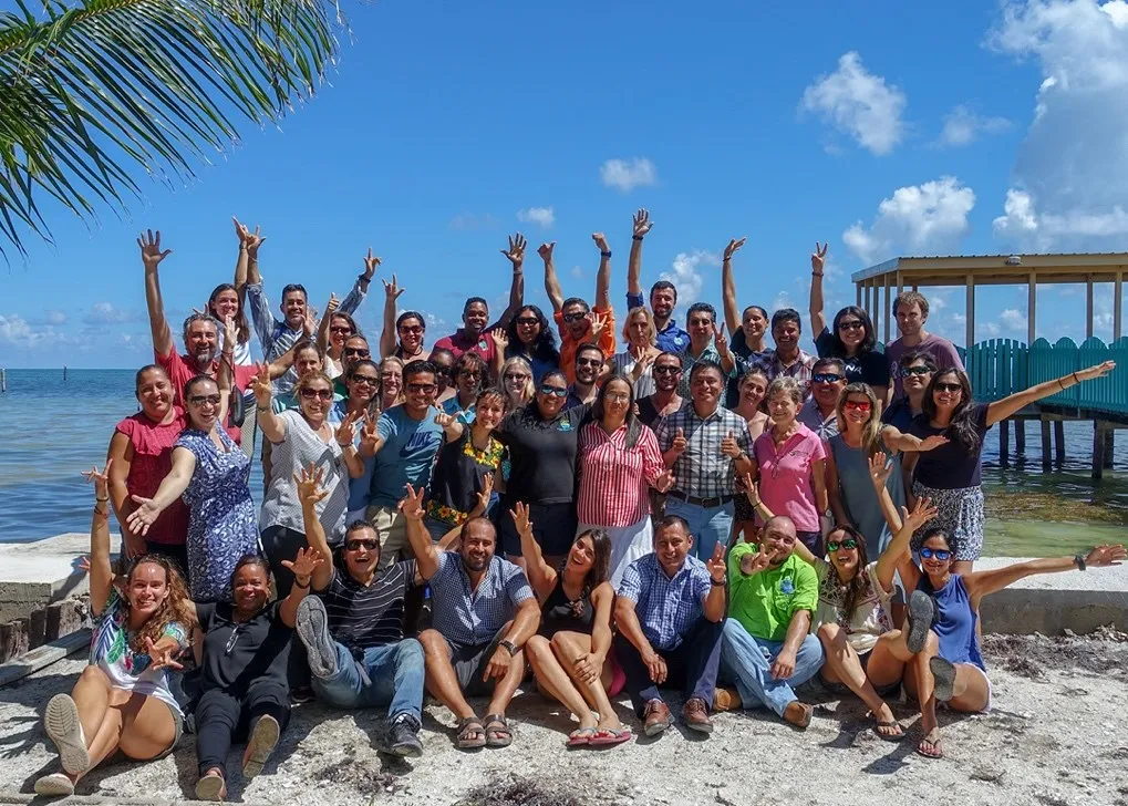 a group of people next to a covered blue dock on a sunny beach wave to the camera