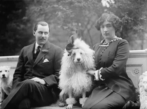A light-skinned man and woman sit on a bench with a white dog between them