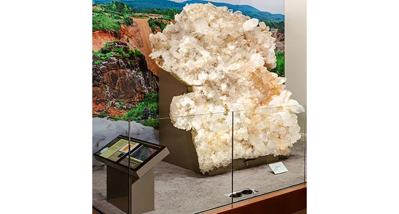 Huge cluster of sparkling white and clear quartz crystals on a museum display platform.