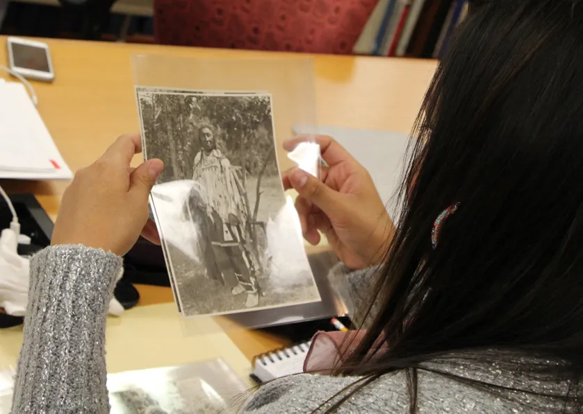 Woman looking at old, archival photograph of a man in traditional Apsaalooke (Crow) clothing