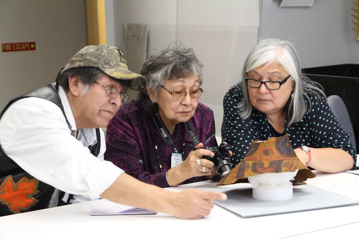 Three Tlingit tribal elders examine traditional hat in collections