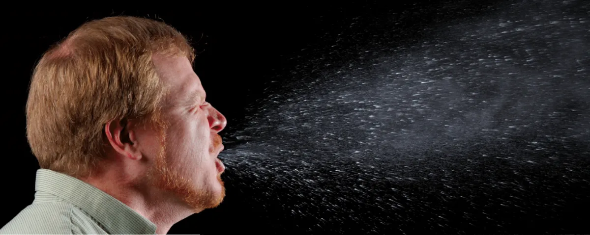 a man against black background sneezes and see particles 