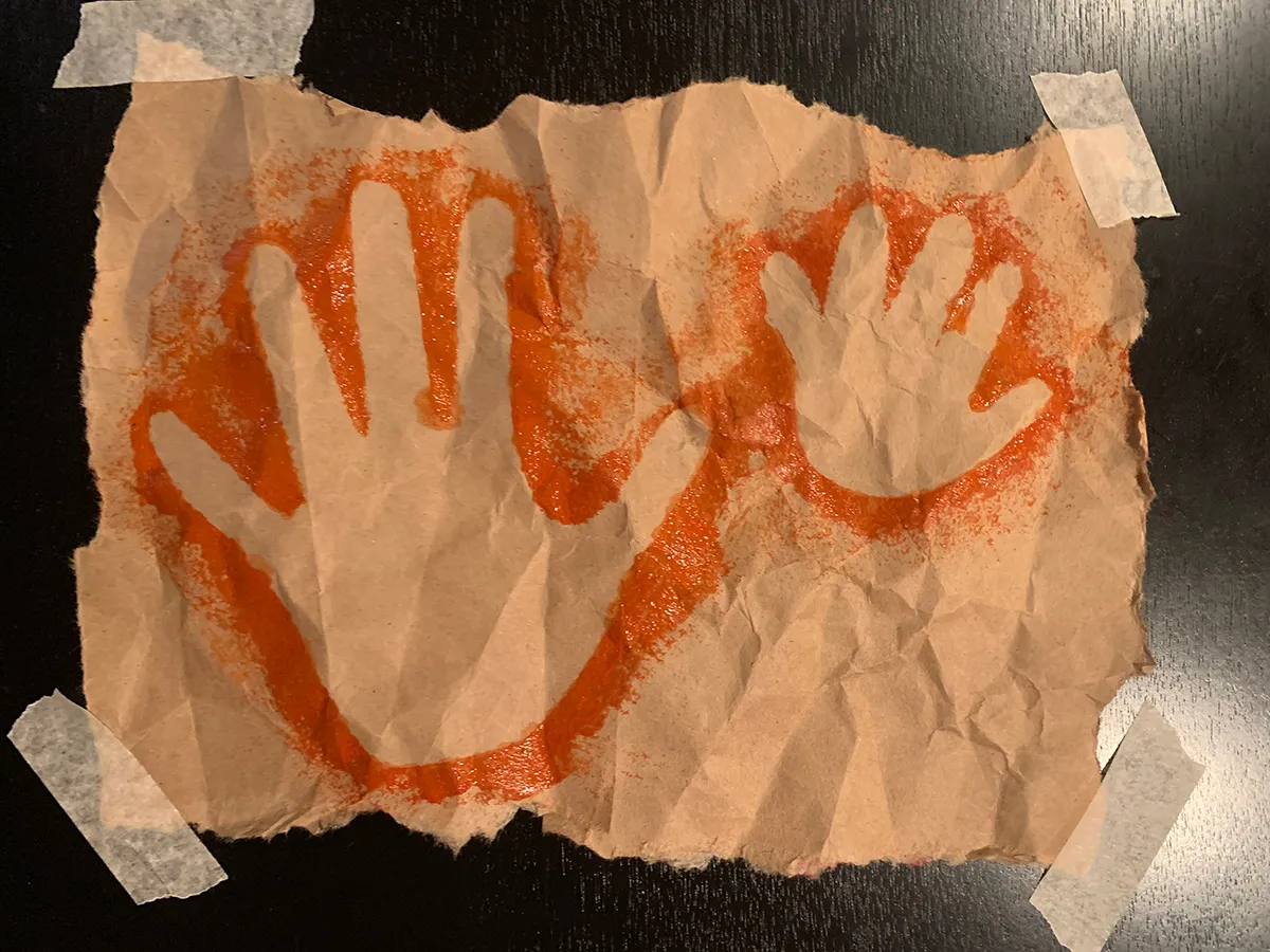 Red-orange outlines of two human handprints on brown paper.