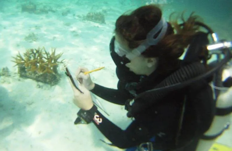 A woman in scuba gear underwater, writing on a clipboard.