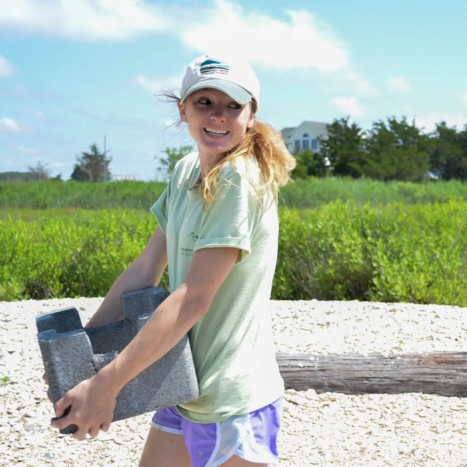 A woman wearing a baseball cap, carrying what looks like a cinder block.